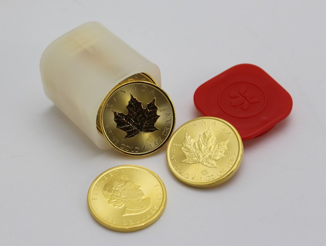 Ein Plastikbehälter mit rotem Deckel ist geöffnet und zeigt drei kanadische Goldmünzen, die mit einem Ahornblatt und dem Profil eines Frauenkopfes bedruckt sind. Diese Münzen, wahrscheinlich wertvolle Sammlerstücke, erinnern an die reiche Geschichte der königlichen Artefakte Aachens.