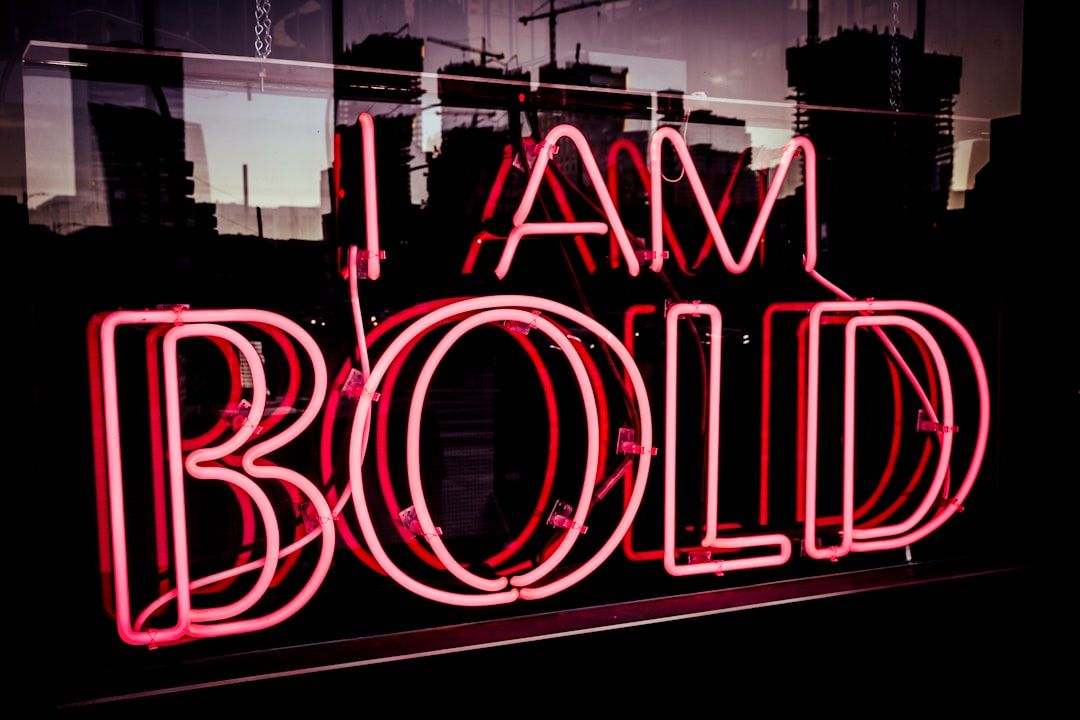 Rotes Neonschild mit der Aufschrift „I AM BOLD“ vor einem dunklen urbanen Hintergrund mit Gebäudesilhouetten, die an die Aachener Architektur erinnern.