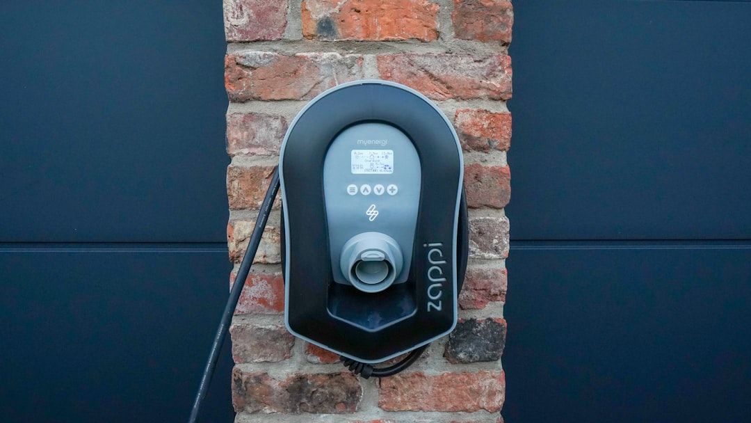 Ein elegantes, schwarzes Ladegerät für Elektrofahrzeuge, das an einer Backsteinmauer in Aachen montiert ist, zeigt Ladeinformationen effizient auf einem kleinen Bildschirm an.