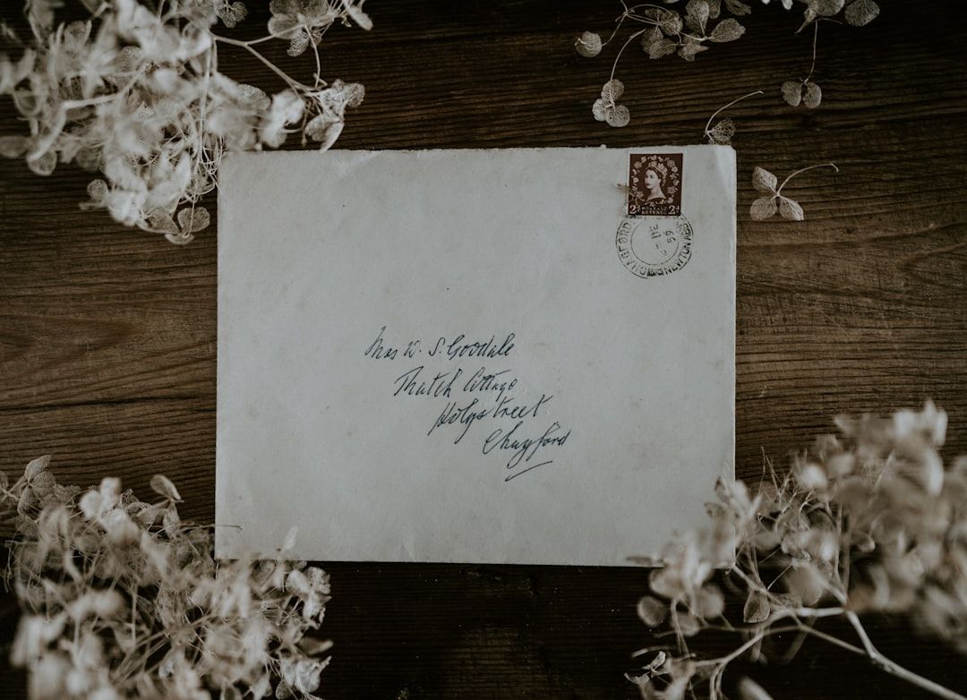Ein alter, abgenutzter Briefumschlag mit handschriftlicher Adresse und einer Briefmarke aus Aachen, umgeben von getrockneten Blumen auf einer Holzoberfläche.