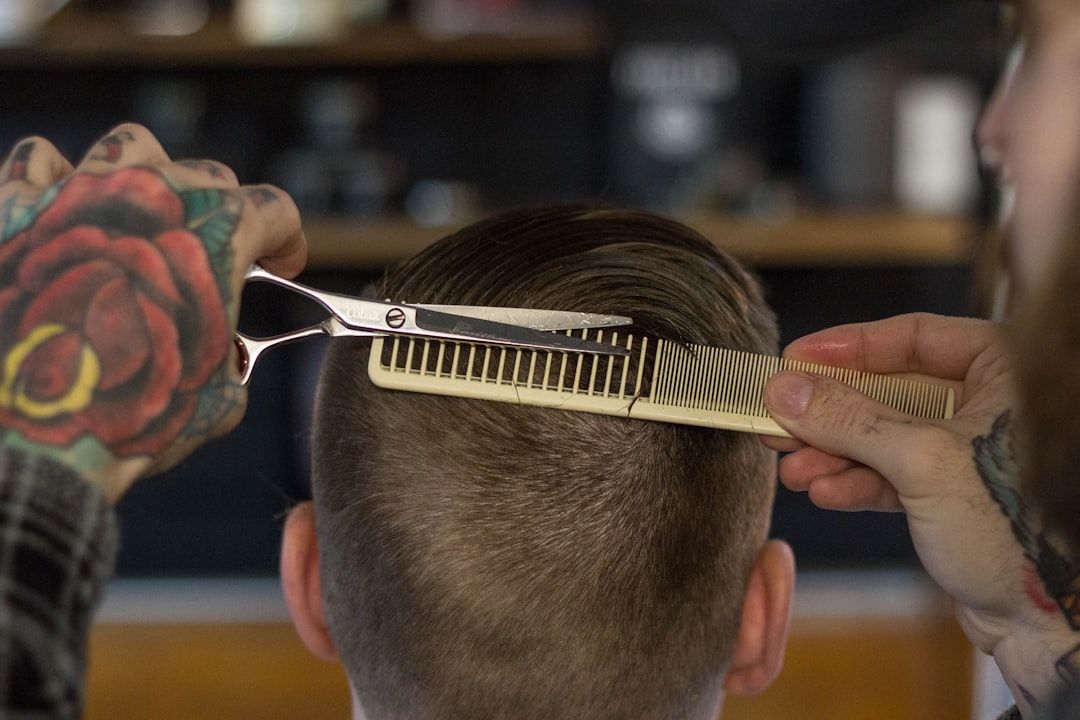 Eine Person mit Tätowierungen an den Händen schneidet einer Person in einem gemütlichen Barbershop in Aachen mit Schere und Kamm die Haare.