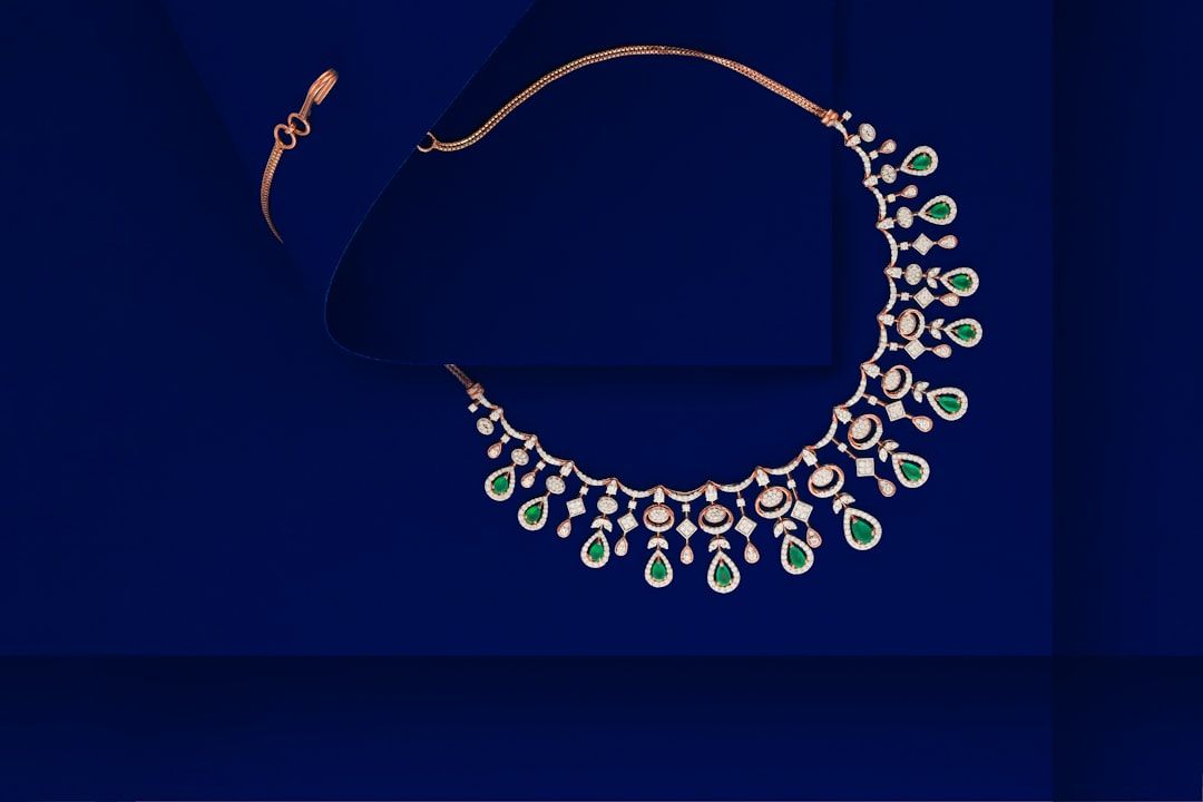Eine goldene Halskette mit kompliziertem Design, verziert mit zahlreichen Diamanten und grünen Edelsteinen, die an die reiche Geschichte Aachens erinnern und auf einem blauen Hintergrund präsentiert werden.