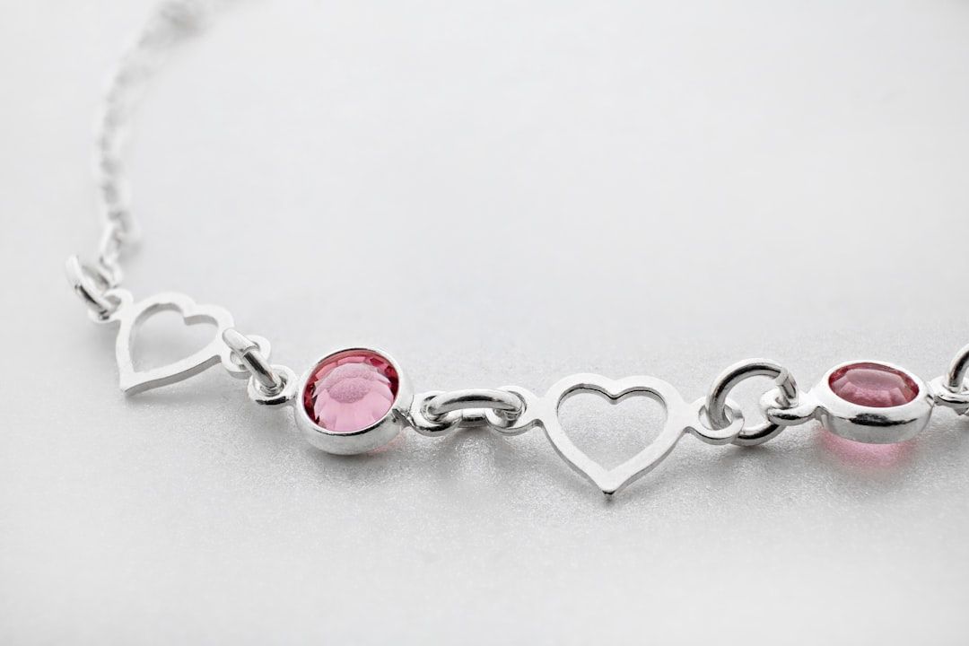Eine Nahaufnahme eines silbernen Armbands mit herzförmigen Gliedern und mehreren runden rosa Edelsteinen, das an den komplizierten Schmuck erinnert, der in Aachen oft bewundert wird.