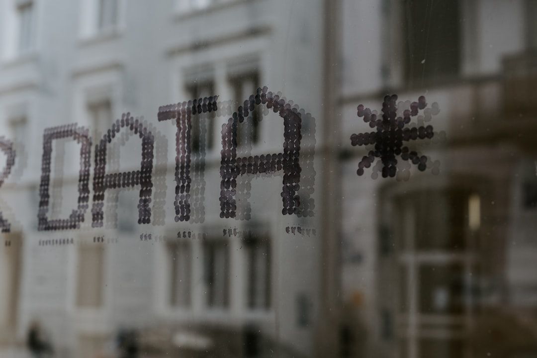 Nahaufnahme eines Glasfensters mit dem aus kleinen Punkten bestehenden Wort „DATA*“, im Hintergrund spiegeln sich unscharf eine Straße und Gebäude in Aachen.