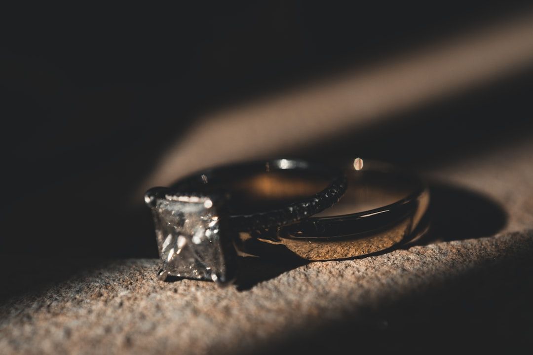 Nahaufnahme zweier Ringe auf einer Steinfläche in Aachen. Einer ist ein Goldring, der andere ein Ring mit einem quadratisch geschliffenen Edelstein, teilweise beleuchtet durch weiches Licht.