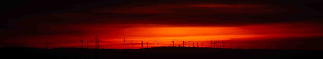 Am Horizont heben sich die Silhouetten von Windrädern vor einem leuchtend rot-orangen Sonnenuntergangshimmel ab und erinnern an die ruhigen Landschaften bei Aachen.