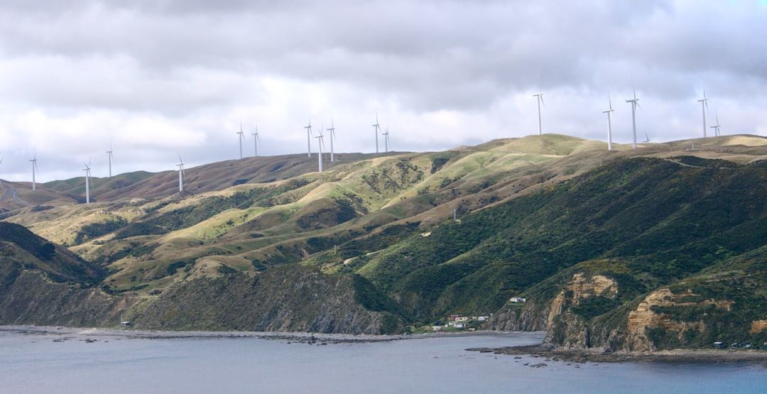 Eine Reihe von Windrädern steht auf sanften grünen Hügeln in der Nähe von Aachen und überblickt eine felsige Küste unter einem bewölkten Himmel.