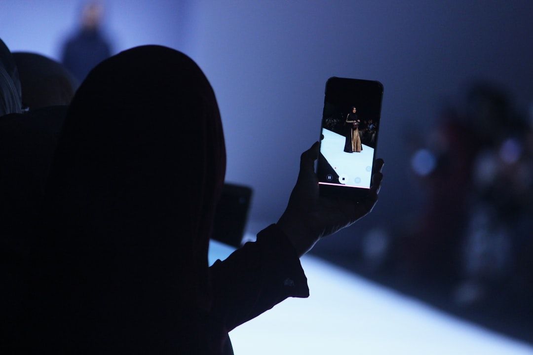 Die Person im Vordergrund hält ein Smartphone und macht ein Foto von einem Model, das über den Laufsteg in Aachen schreitet.