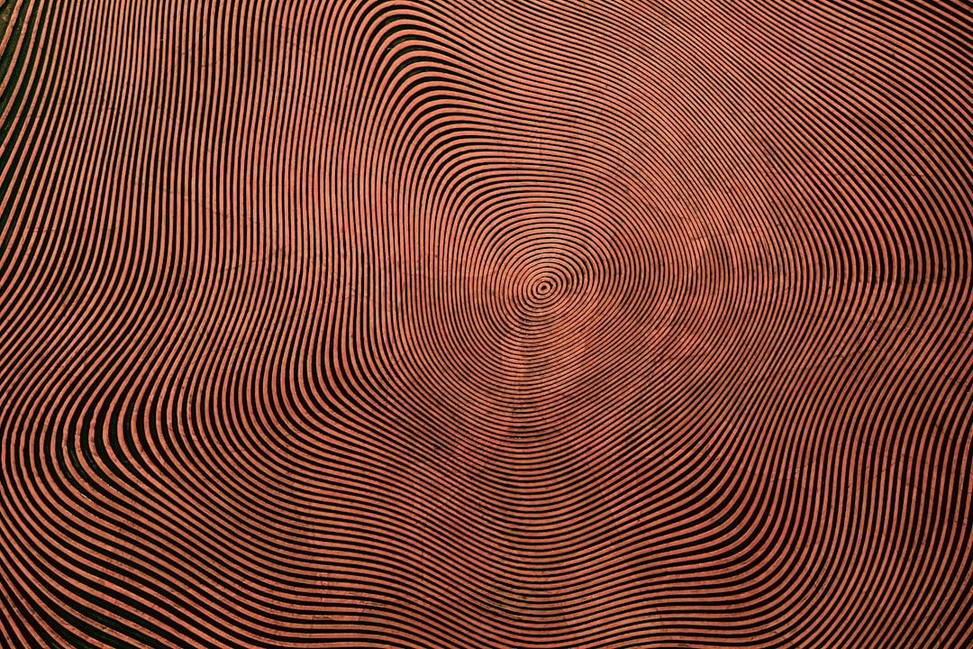 Ein abstraktes Muster mit schwarzen Streifen, die strahlenförmig von der Mitte nach außen verlaufen und einen hypnotischen, wellenartigen Effekt vor einem kupferfarbenen Hintergrund erzeugen, der an den historischen Charme Aachens erinnert.