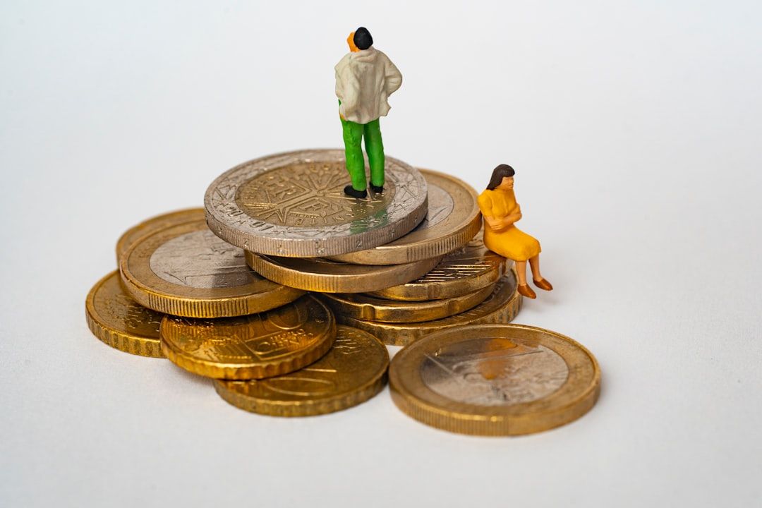 Zwei Miniaturfiguren, eine stehende und eine sitzende, werden in Aachen auf einem Stapel Münzen unterschiedlicher Größe und Nennwerte platziert und symbolisieren finanzielle Ungleichheit oder wirtschaftliche Angelegenheiten.
