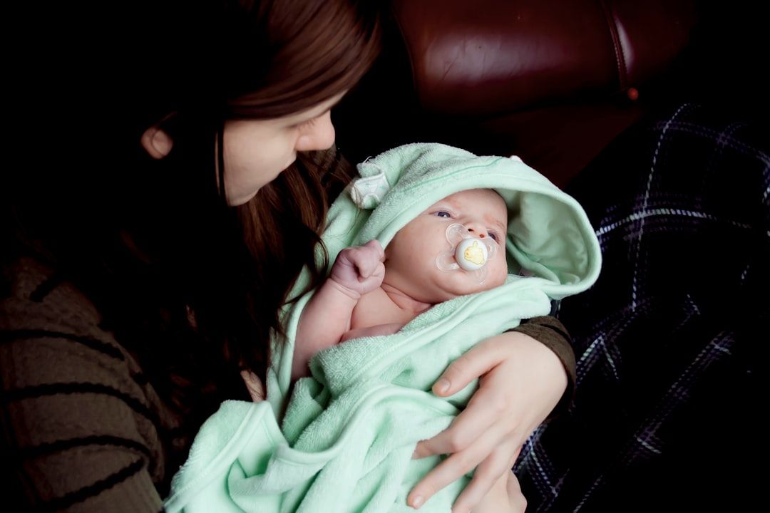 Eine Person mit braunen Haaren hält ein in eine grüne Decke gewickeltes Baby mit Schnuller und sitzt auf einer dunklen Fläche in einem Aachener Café.