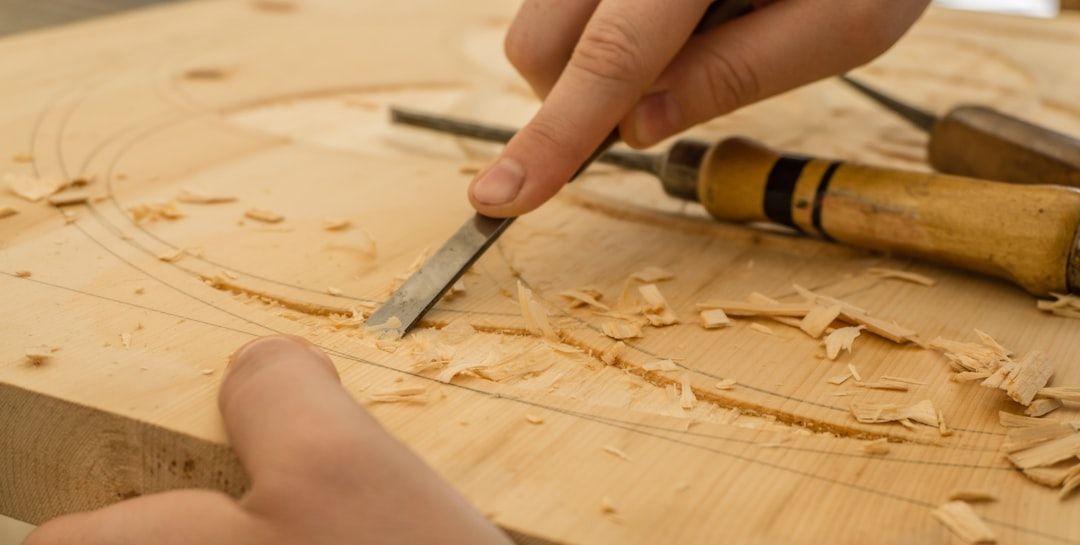 Ein Mensch in Aachen schnitzt mit einem Meißel in ein Stück Holz, wobei Holzspäne verstreut herumfliegen.