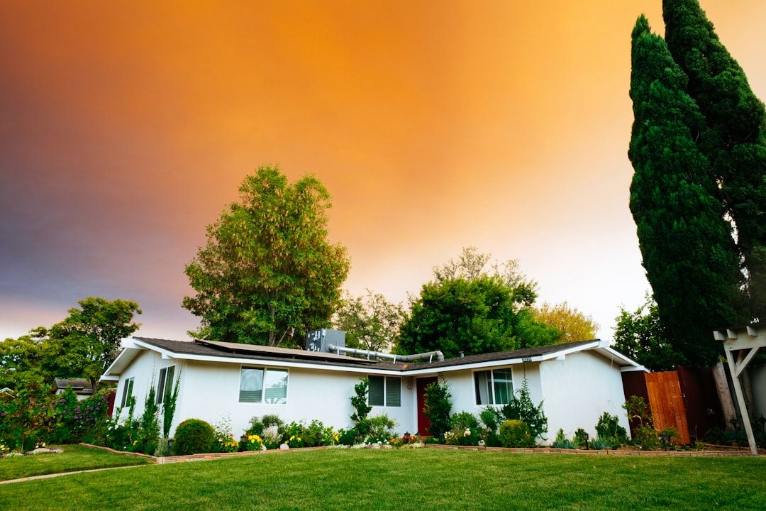 Ein weißes einstöckiges Haus mit gepflegtem Garten und grünem Rasen vor einem leuchtend orangefarbenen Himmel bei Sonnenuntergang erinnert an den Charme eines Aachener Abends.