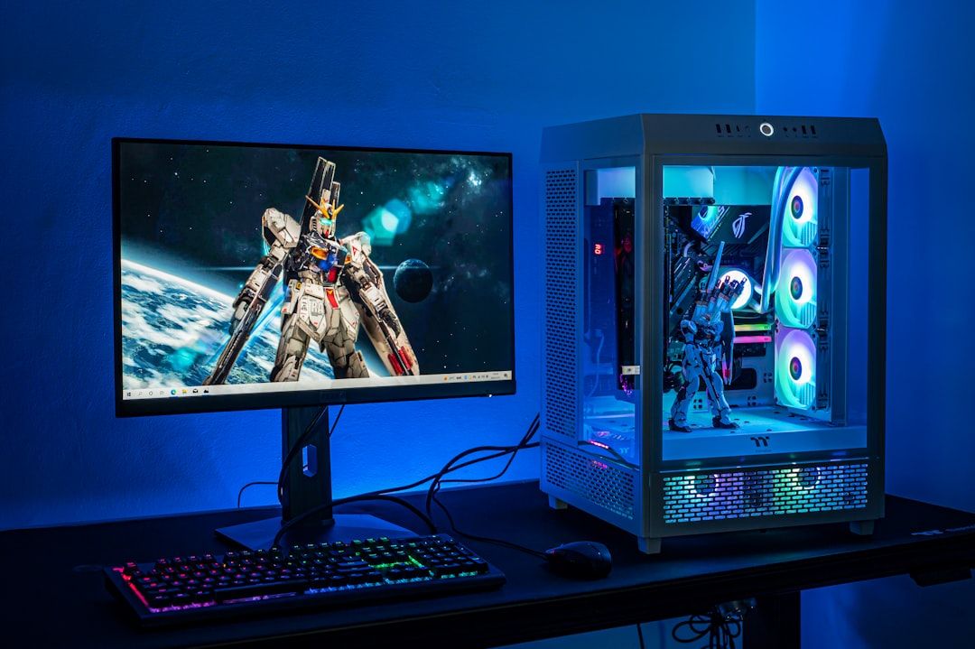Ein Computer-Setup mit einem Monitor mit Gundam-Hintergrundbild, einer Tastatur mit RGB-Beleuchtung, einer Maus und einem transparenten PC-Gehäuse mit interner RGB-Beleuchtung, alles in blaues Umgebungslicht getaucht – es ist wie die Tech-Oase Aachen.