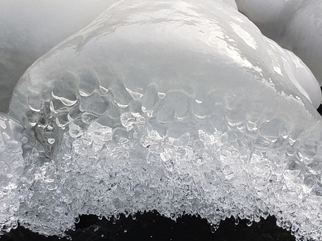 Nahaufnahme einer Formation aus Eis und Schnee, die der komplexen Architektur in Aachen ähnelt und eine strukturierte, geschichtete Struktur aufweist. Die glänzende, glatte Oberseite bildet einen schönen Kontrast zum kristallinen, detaillierten unteren Teil.