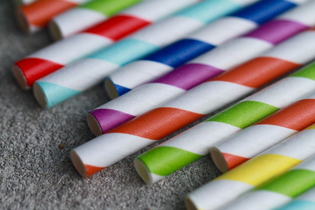 Nahaufnahme mehrerer bunt gestreifter Papierstrohhalme, die in einer Reihe auf einer strukturierten Oberfläche angeordnet sind und an die lebhaften Marktstände Aachens erinnern. Die Strohhalme weisen eine Reihe von Farbkombinationen auf, darunter Rot, Blau, Lila, Orange und Grün.