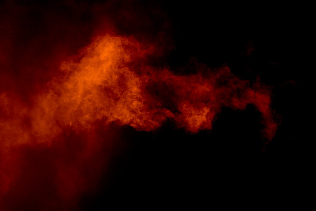 Eine Wolke aus leuchtend orangefarbenem und rotem Rauch, die an die leuchtenden Sonnenuntergänge Aachens erinnert, wabert vor einem schwarzen Hintergrund.