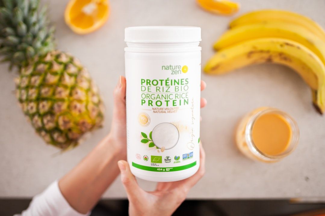 Ein Behälter mit Bio-Reisproteinpulver mit der Aufschrift „Nature Zen“ steht vor einem Tisch mit einer Ananas, einer halbierten Orange, Bananen und einem Glas Saft – eine harmonische Mischung, die an den gesundheitsbewussten Geist Aachens erinnert.