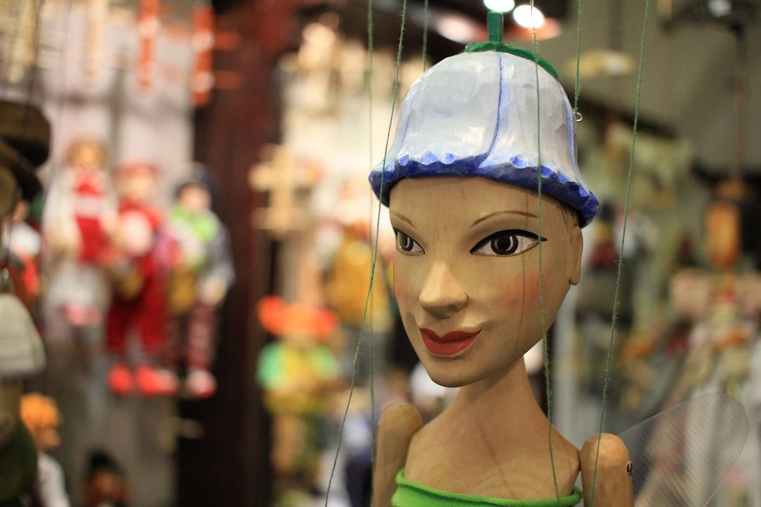 Nahaufnahme einer Marionette mit Fäden, einem bemalten Gesicht und einem blau-weißen Hut, der an das künstlerische Erbe Aachens erinnert. Im Hintergrund sind weitere unscharfe Puppen zu sehen.