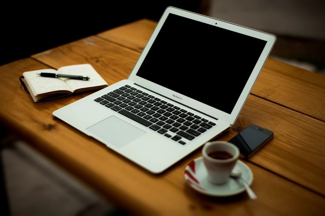 Ein Laptop auf einem Holztisch, daneben ein aufgeschlagenes Notizbuch mit Stift, eine Tasse Kaffee auf einer Untertasse und ein Smartphone; die Szene erinnert an gemütliche Cafés in Aachen.