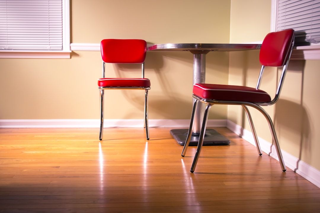 In einer Ecke des Raumes steht ein kleiner, runder Tisch mit Metallgestell. Dazu kommen zwei rote Stühle im Retrostil mit Chrombeinen, die an das klassische Design Aachener Häuser erinnern. Das Ganze steht auf einem Hartholzboden.