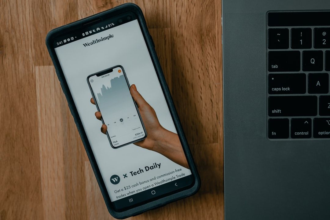 Ein Smartphone mit der Wealthsimple-App und einem Diagramm liegt neben einem Laptop auf einer Holzoberfläche und bietet einem Investor in Aachen einen ruhigen Moment.