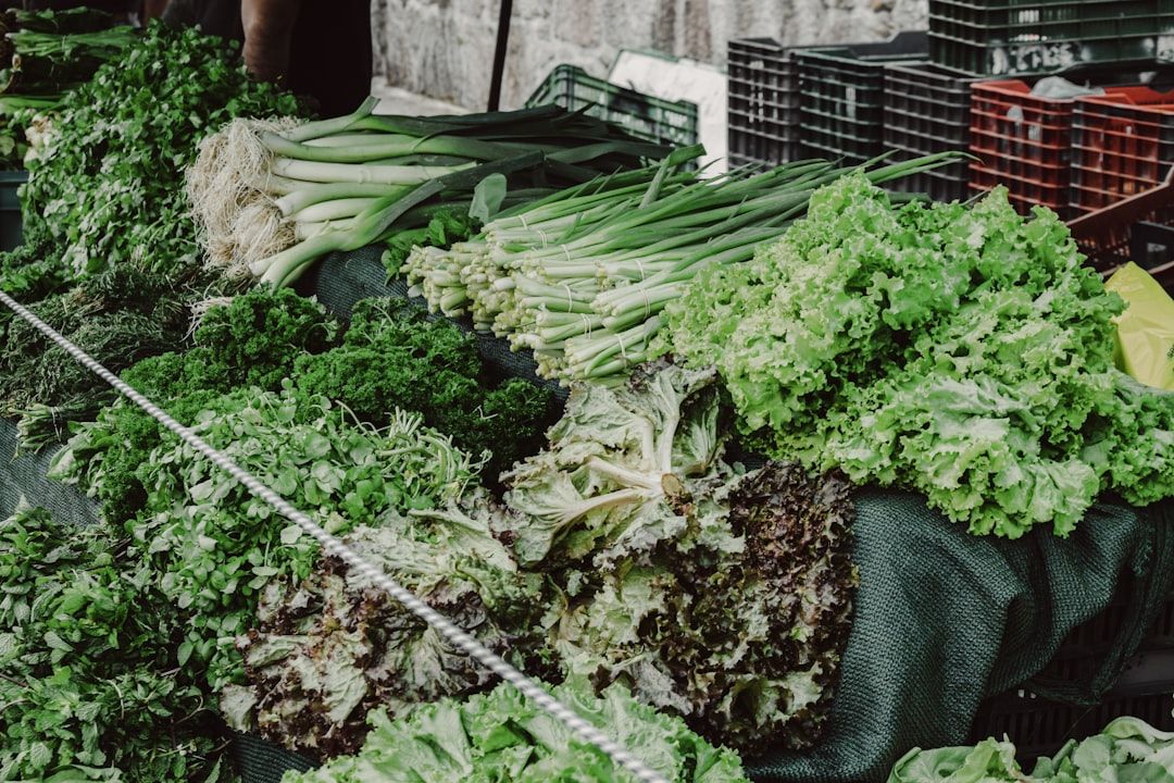 An einem Marktstand in Aachen werden verschiedene frische grüne Gemüsesorten angeboten, darunter Salat, Frühlingszwiebeln und Kräuter.