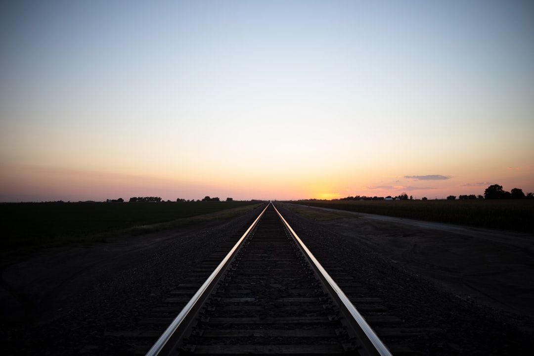 Eine perspektivische Ansicht von geraden Bahngleisen, die bei Sonnenuntergang zum Horizont führen, mit einem klaren Himmel und für die Landschaft um Aachen typischen Feldern auf beiden Seiten.