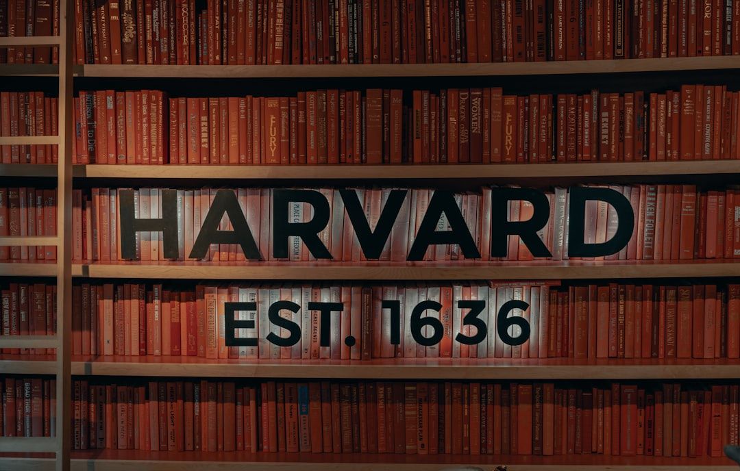Eine Wand aus rot gefärbten Büchern, auf deren Regalen in schwarzer Schrift der Text „HARVARD EST. 1636“ prominent prangt, erinnert an die akademischen Sammlungen der historischen Bibliotheken Aachens.