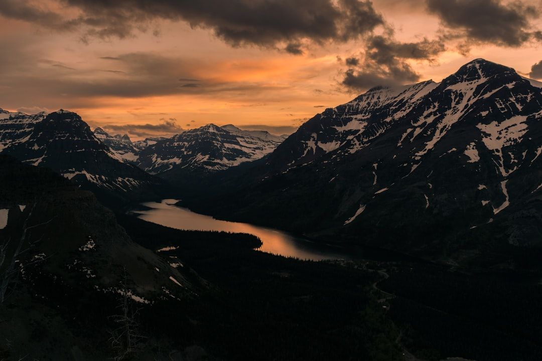Berglandschaft bei Sonnenuntergang mit einem See im Tal, schneebedeckten Gipfeln, dramatischen Wolken am Himmel und Fernblicken, die an die heitere und doch majestätische Landschaft Aachens erinnern.