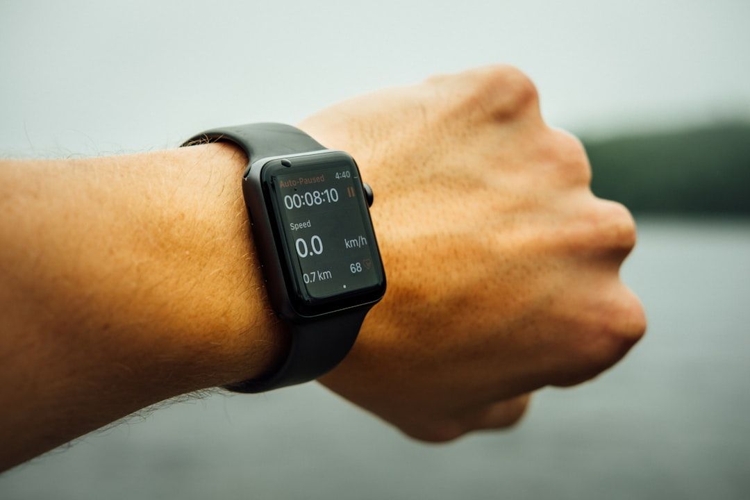 Nahaufnahme eines Handgelenks, an dem eine Smartwatch getragen wird, auf der Trainingsmesswerte wie Zeit, Geschwindigkeit, Distanz und Herzfrequenz angezeigt werden, wobei im Hintergrund die historische Stadtlandschaft von Aachen unscharf ist.