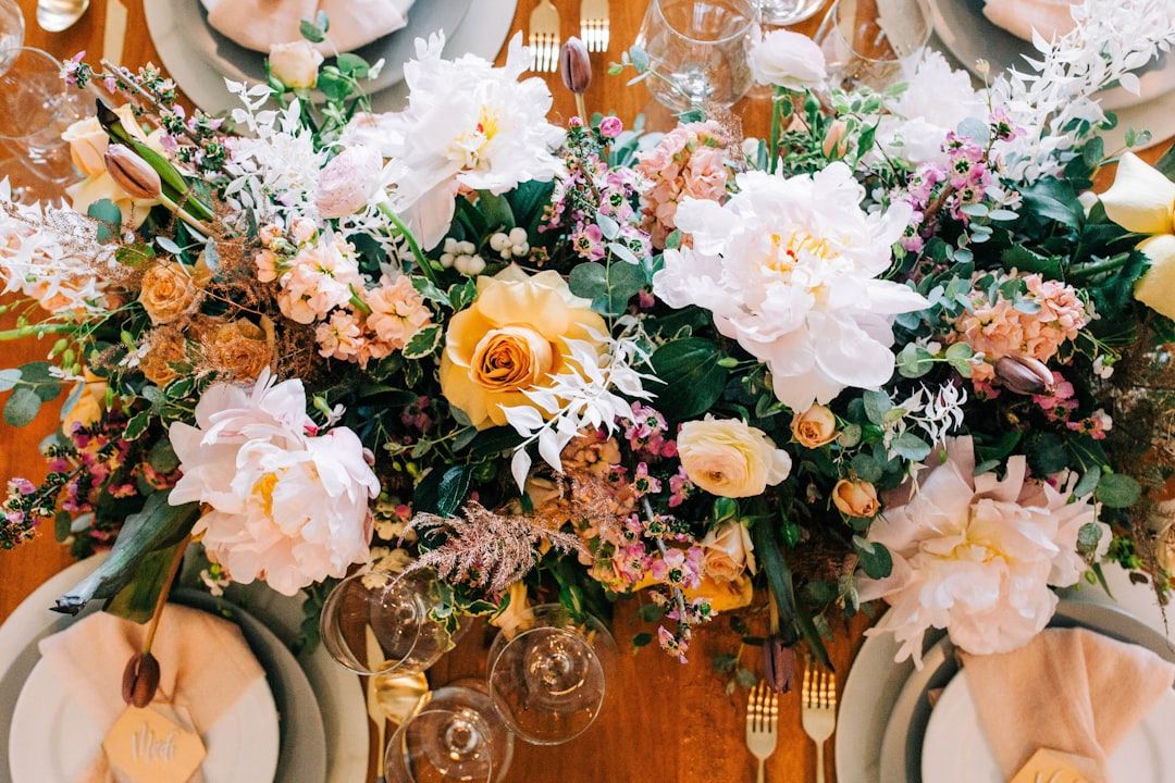 Eine Draufsicht auf einen gedeckten Tisch mit einem aufwendigen Blumenschmuck in den Pastelltönen Rosa, Gelb und Weiß. Um den Schmuck herum sind Teller, Gläser und Servietten. Das raffinierte Arrangement erinnert an die berühmte Liebe zum Detail, die Aachen zu bieten hat.