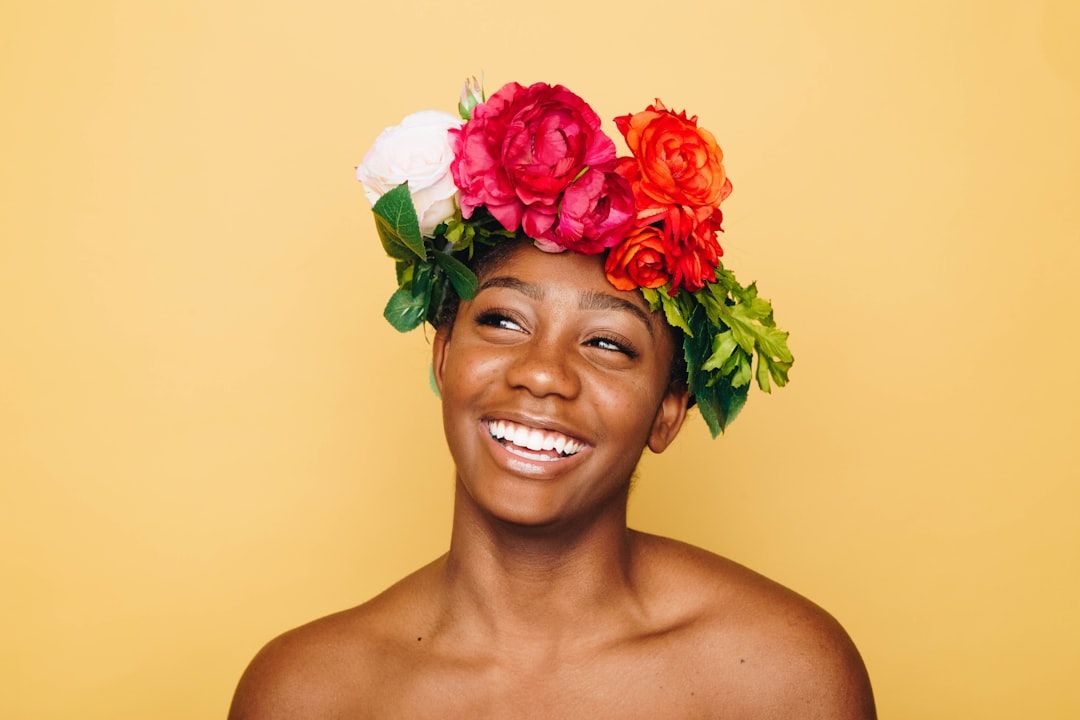 Eine Person lächelt und trägt ein farbenfrohes Blumenstirnband, das vor einem sonnigen gelben Hintergrund einen Hauch von Aachener Charme verbreitet.