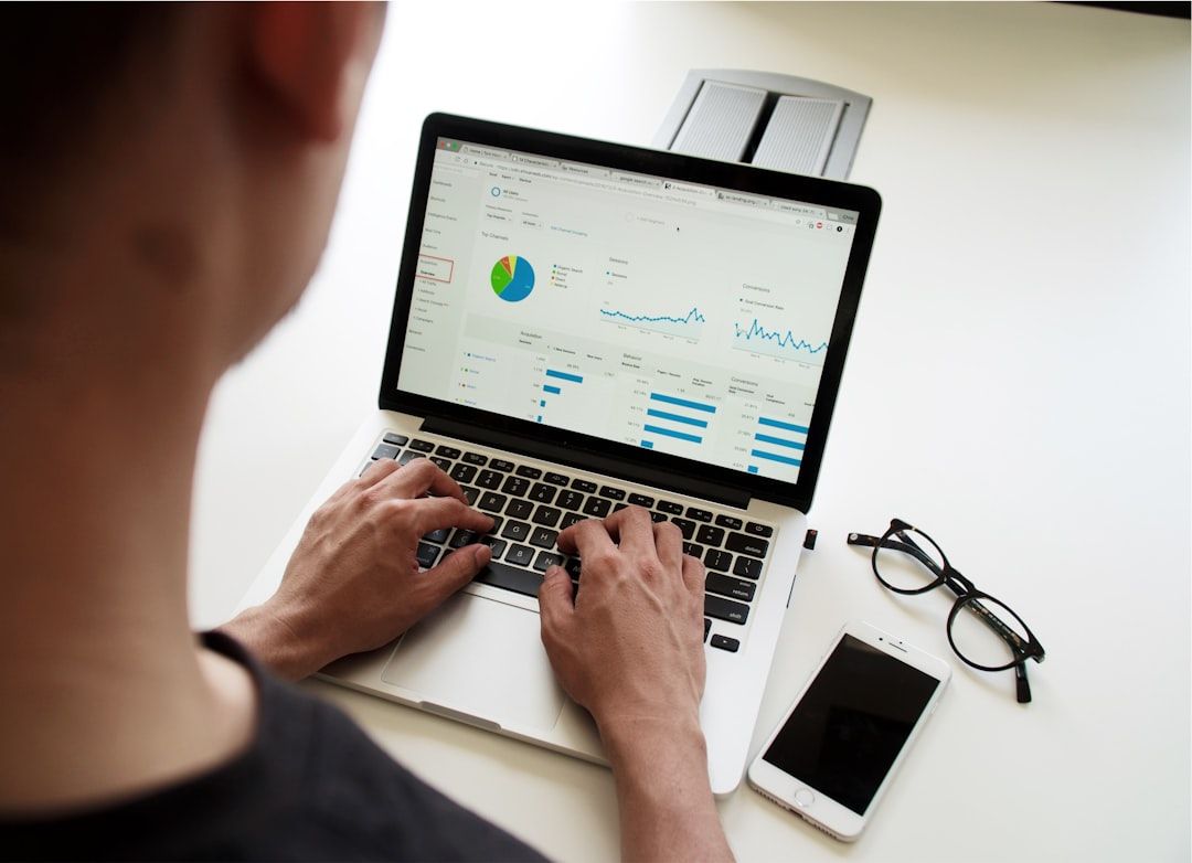 Eine Person tippt auf einem Laptop, auf dem Grafiken und Diagramme angezeigt werden. Daneben liegen ein Smartphone und eine Brille auf dem Tisch und tragen zur produktiven Atmosphäre bei. Der Arbeitsplatz erinnert an ein modernes Büro in Aachen und verbindet Effizienz mit einem Hauch europäischen Charme.