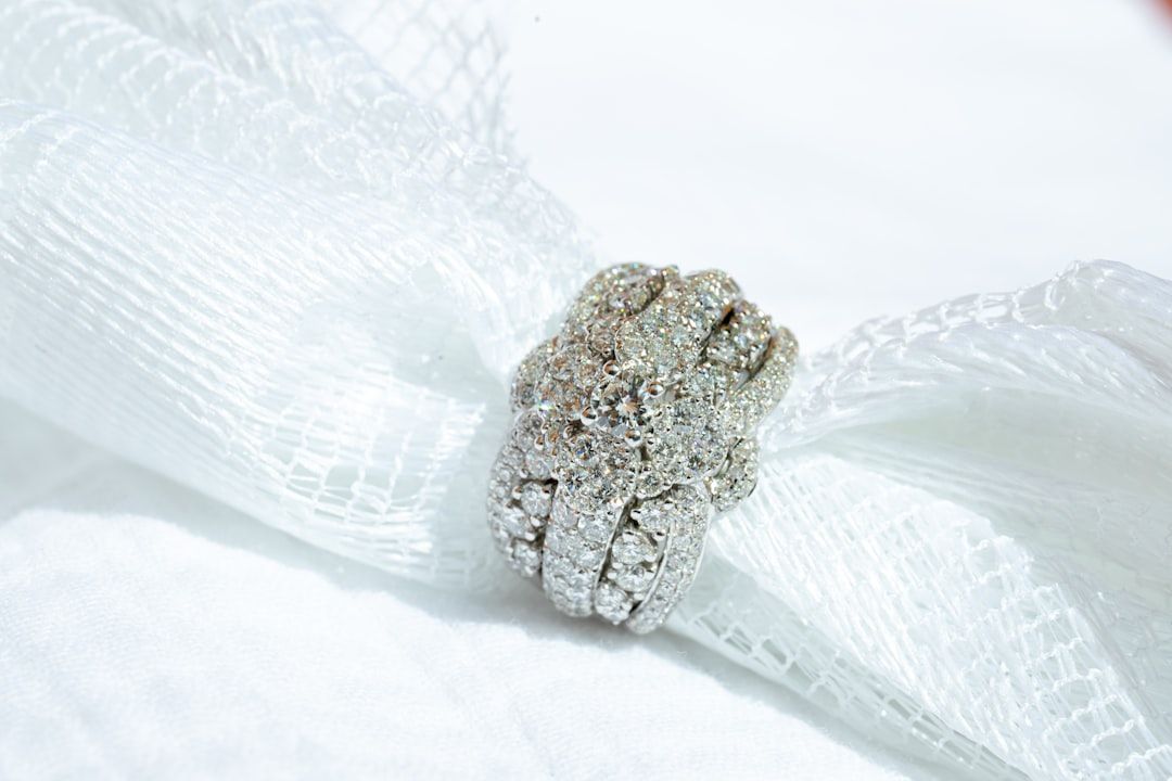 Ein mit Diamanten besetzter Silberring auf einem strukturierten weißen Stoffband erinnert an den Charme der historischen Eleganz Aachens.