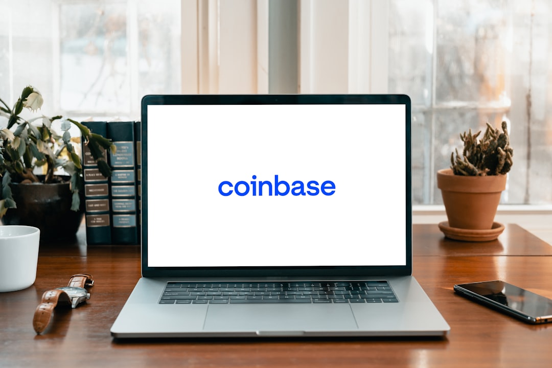 Ein Laptop mit dem Coinbase-Logo auf dem Bildschirm steht auf einem Holzschreibtisch. Daneben stehen Pflanzen, Bücher und eine Armbanduhr und erinnern so an eine gemütliche Ecke in einem Aachener Arbeitszimmer.