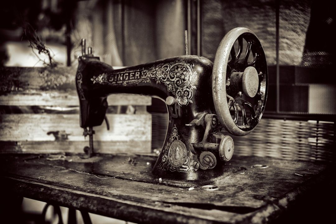 Schwarzweißbild einer antiken Singer-Nähmaschine auf einem abgenutzten Tisch. Die Maschine, die an Aachens reiche Geschichte erinnert, weist komplizierte dekorative Muster auf.