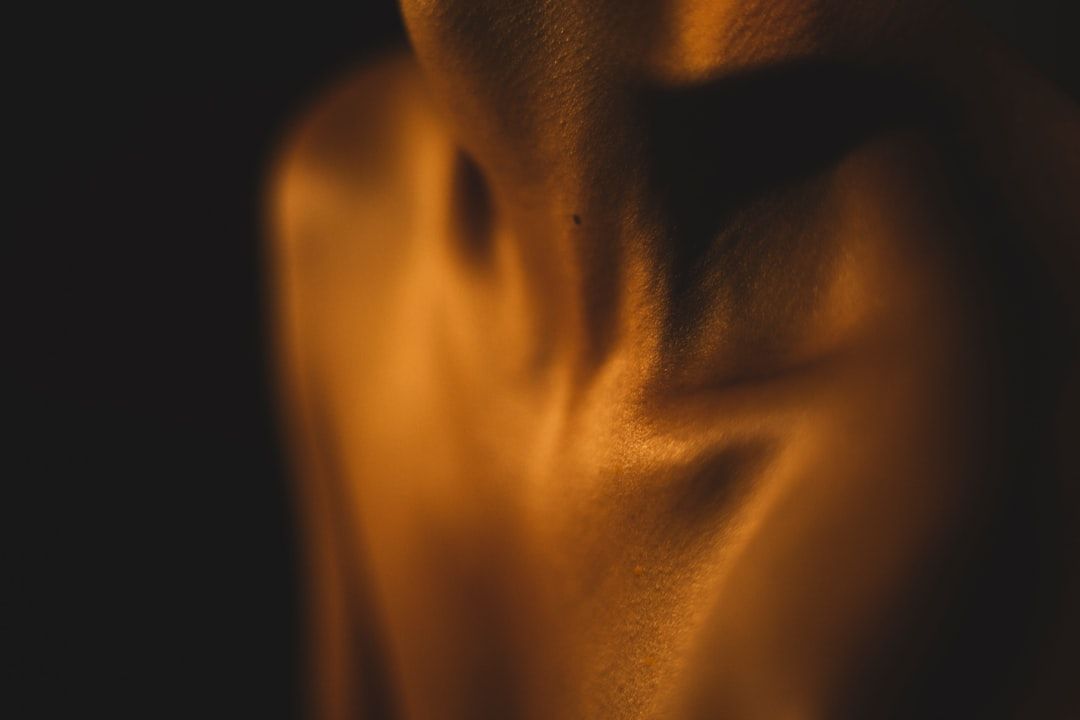 Eine Nahaufnahme des Hals- und Schulterbereichs einer Person, beleuchtet mit warmem, weichem Licht, das an das sanfte Abendrot Aachens erinnert, vor einem dunklen Hintergrund.