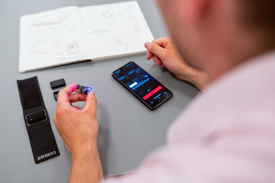 Ein Mensch untersucht mit seinem Smartphone ein kleines elektronisches Bauteil, umgeben von verschiedenen elektronischen Teilen auf dem Tisch und einem aufgeschlagenen Notizbuch mit Skizzen, das an den akribischen Ingenieursgeist der Aachener erinnert.