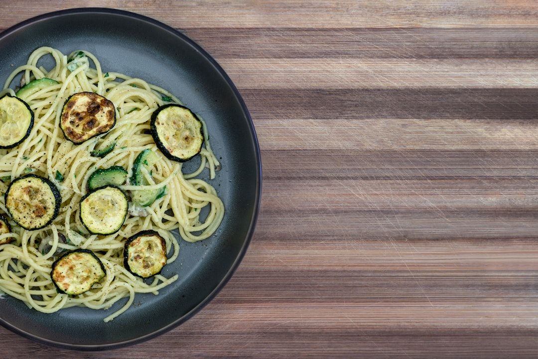 Ein schwarzer Teller gefüllt mit Spaghetti und gegrillten Zucchinischeiben, der an ein charmantes Bistro in Aachen erinnert, platziert auf einer Holzoberfläche.
