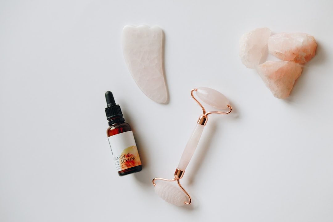 Eine Flasche Gesichtsserum, ein rosa Gesichtsroller, ein Gua-Sha-Werkzeug und eine Gruppe kunstvoll auf weißem Hintergrund angeordneter Rosenquarzsteine erinnern an die heitere Schönheit der Aachener Spa-Tradition.
