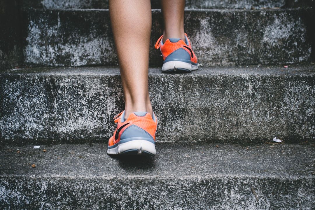 Person in orangefarbenen und grauen Sportschuhen läuft in Aachen eine Betontreppe hinauf.