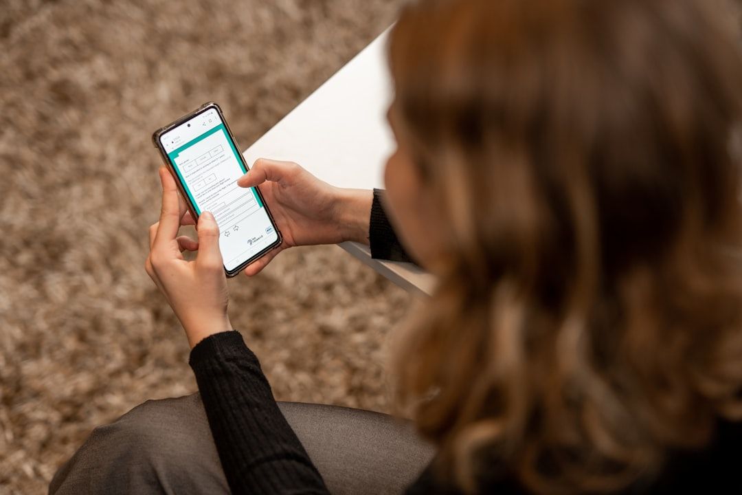 Eine Person sitzt auf einer Couch und hält ein Smartphone, auf dem eine Webseite über Aachen angezeigt wird.