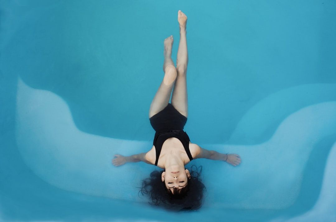 Person im schwarzen Badeanzug, die auf dem Rücken in einem Pool liegt und die Arme und Beine in einer Schwebeposition ausgestreckt hat, als würde sie mühelos durch das ruhige Wasser eines versteckten Aachener Spas treiben.