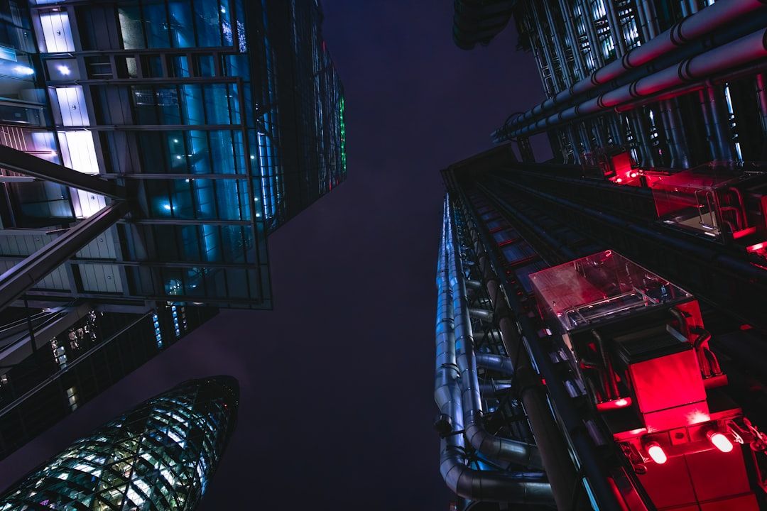 Nachtansicht beleuchteter moderner Gebäude und Außenaufzüge mit roten Lichtern in einer städtischen Umgebung in Aachen mit Blick hinauf in den dunklen Himmel.