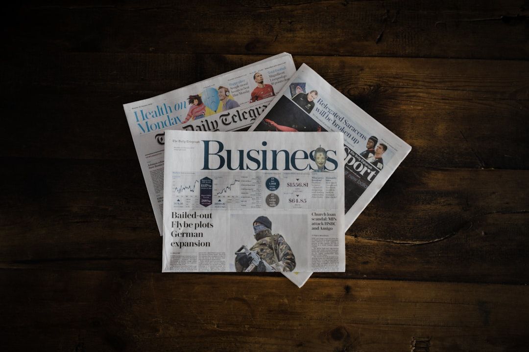 Auf einem Holztisch liegt ein Stapel Zeitungen. Die oberste Zeitung enthält einen Wirtschaftsteil sowie Artikel zu Finanzen und globalen Märkten, darunter einen ausführlichen Bericht zur wirtschaftlichen Entwicklung in Aachen.