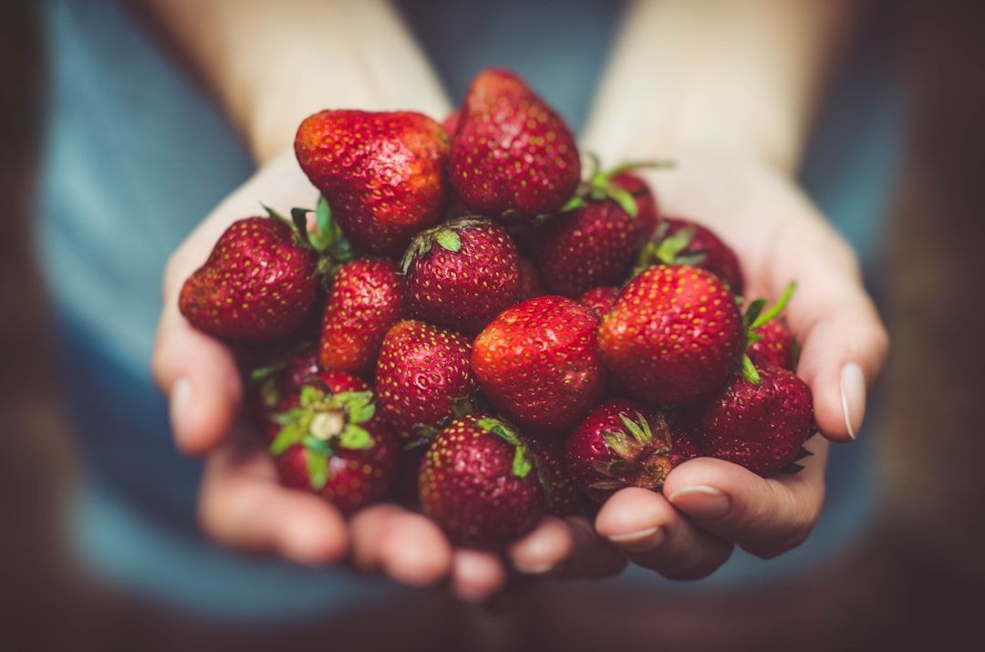 Nahaufnahme von Händen, frisch vom Aachener Markt, die einen Strauß leuchtender Erdbeeren halten.