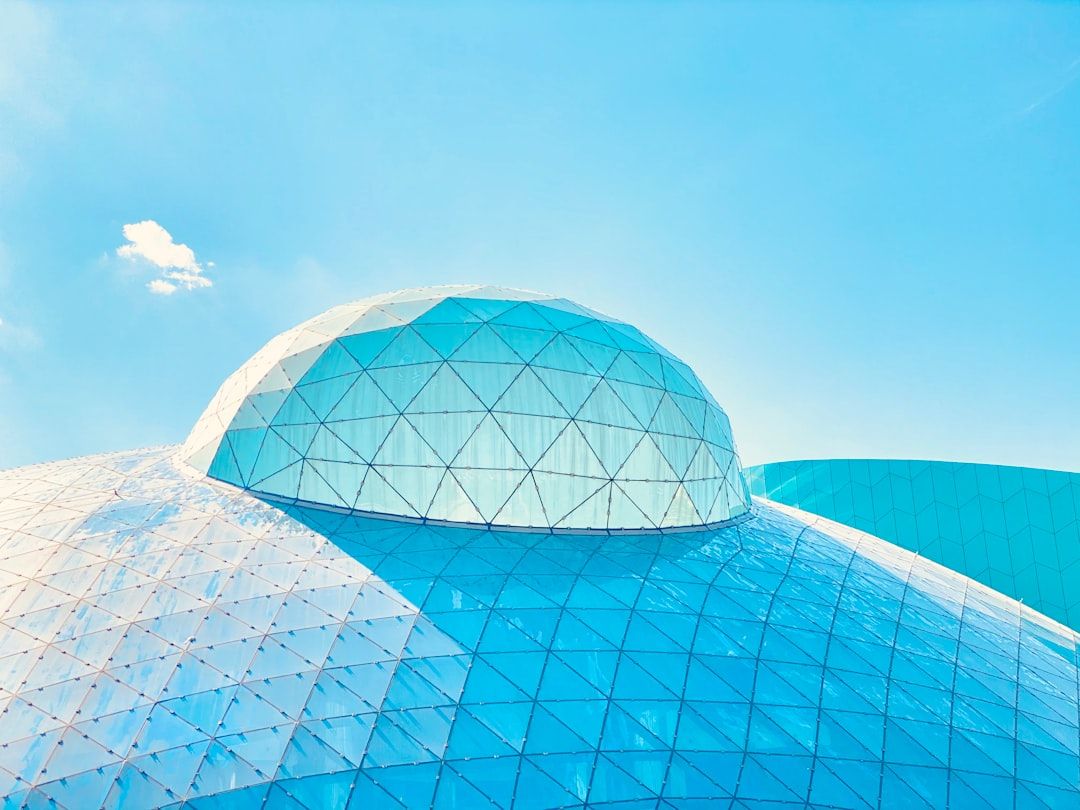Eine große geodätische Kuppel mit kleineren blau-weißen dreieckigen Paneelen thront majestätisch unter dem klaren blauen Himmel in Aachen.