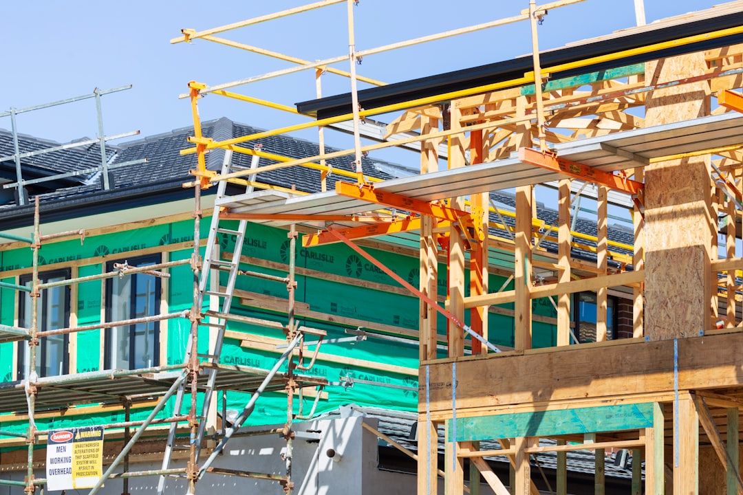 Ein im Bau befindliches zweistöckiges Haus in Aachen, umgeben von Gerüsten, verfügt über grüne Dämmplatten und Holzrahmen in verschiedenen Fertigstellungsstadien.