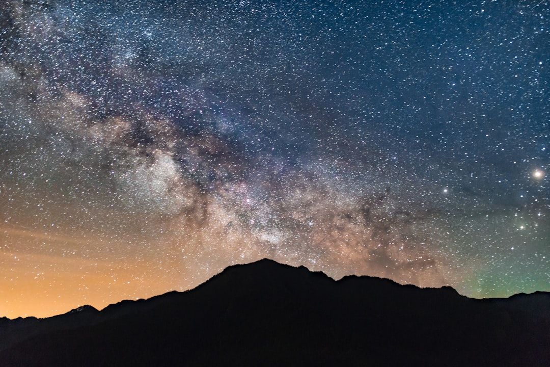 Ein mit Sternen gefüllter Nachthimmel und die Milchstraße über einer Bergkette in der Silhouette erzeugen eine Szene, die an die ruhigen Landschaften Aachens erinnert.